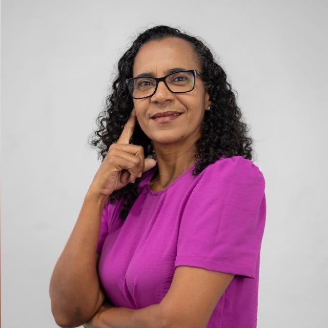 Professora Raquel Rocha, pré-candidata a Deputada Federal, de óculos e blusa rosa, com a mão no queixo